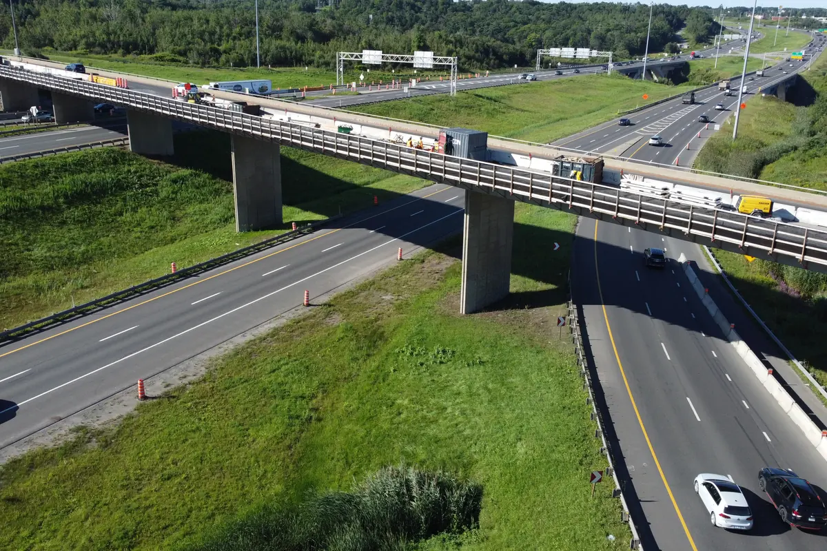 Conteneur, machinerie et matériaux sur le tablier d’un viaduc, circulation maintenue en dessous