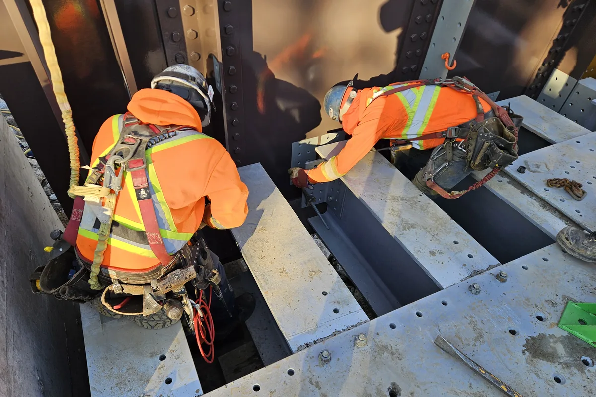 Deux travailleurs en harnais complet, reliés par longe, sur le tablier d’acier d’un pont
